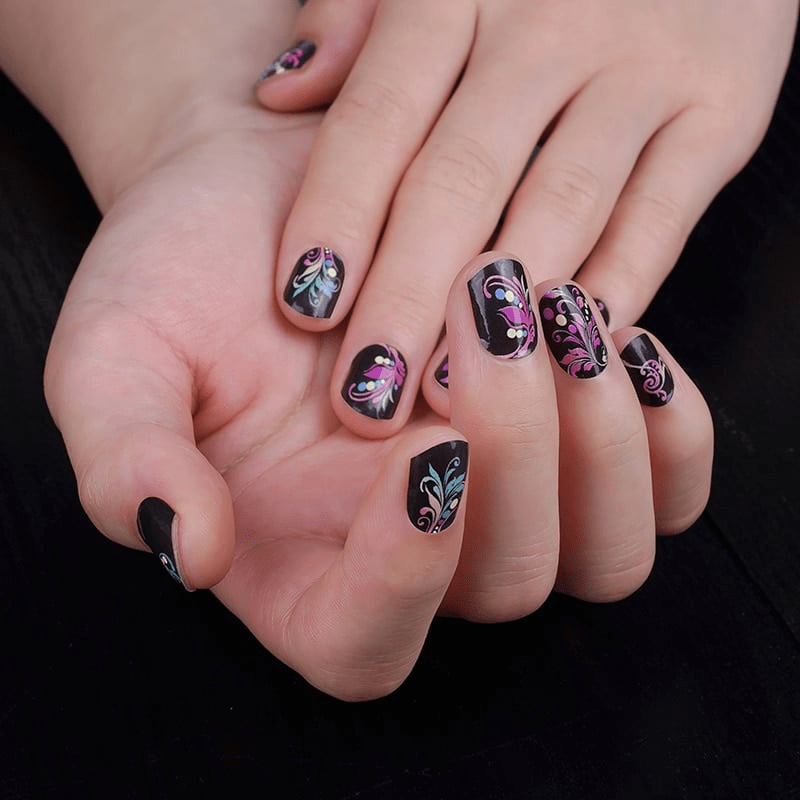 Black nail wraps with pink and teal feather-swirl pattern and white bead accents
