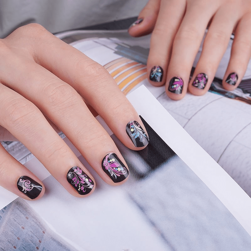 Black nail wraps with ornate pink baroque scrollwork pattern on hands at-home manicure
