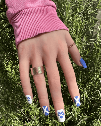 Blue and white Scottish flag nail wraps on hand with pink jumper outdoors