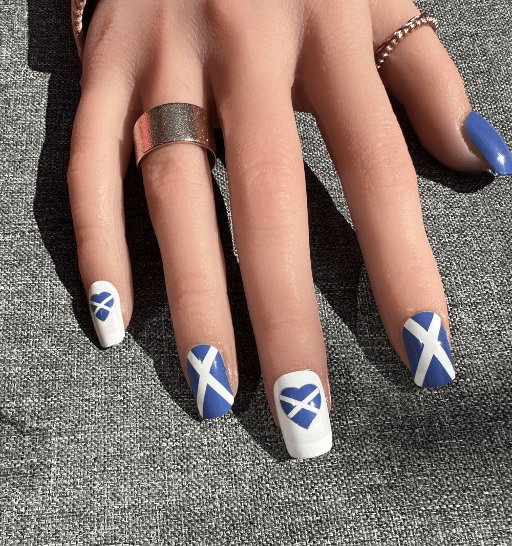 Hand wearing blue and white Scottish flag nail wraps with cross design