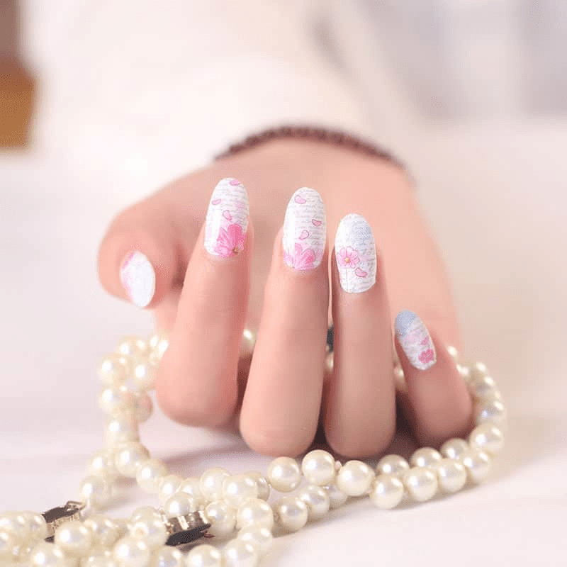 Manicured hand wearing soft pink and blue floral nail wraps with pearl necklace