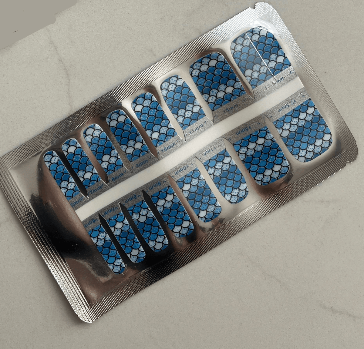 Blue mermaid scale pattern pedicure nail wraps in silver foil packaging