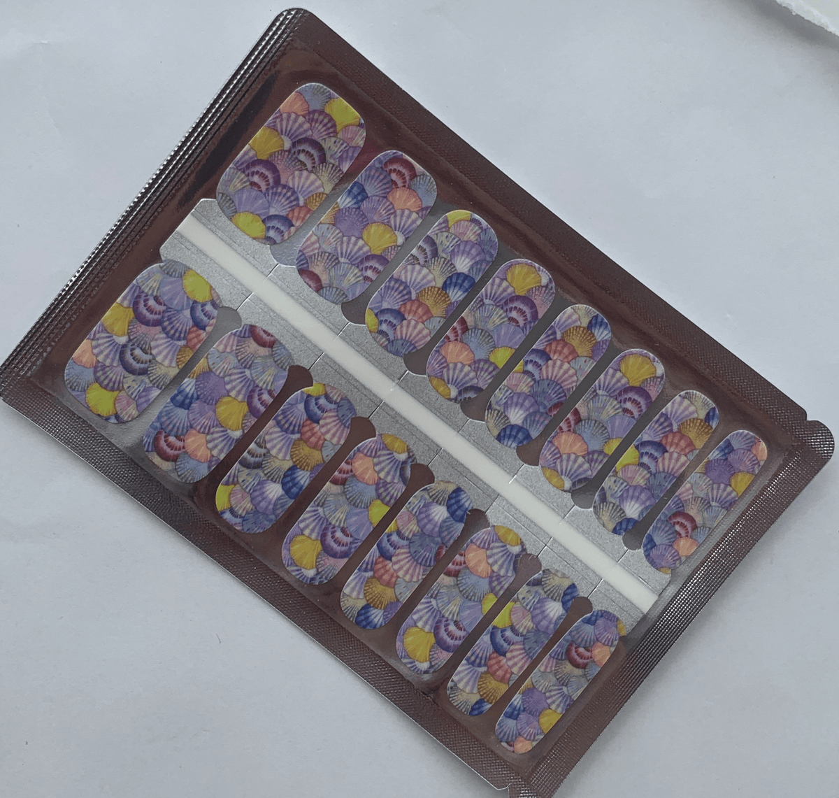 Seashell watercolour nail wraps with pastel purple and yellow ocean design in packaging