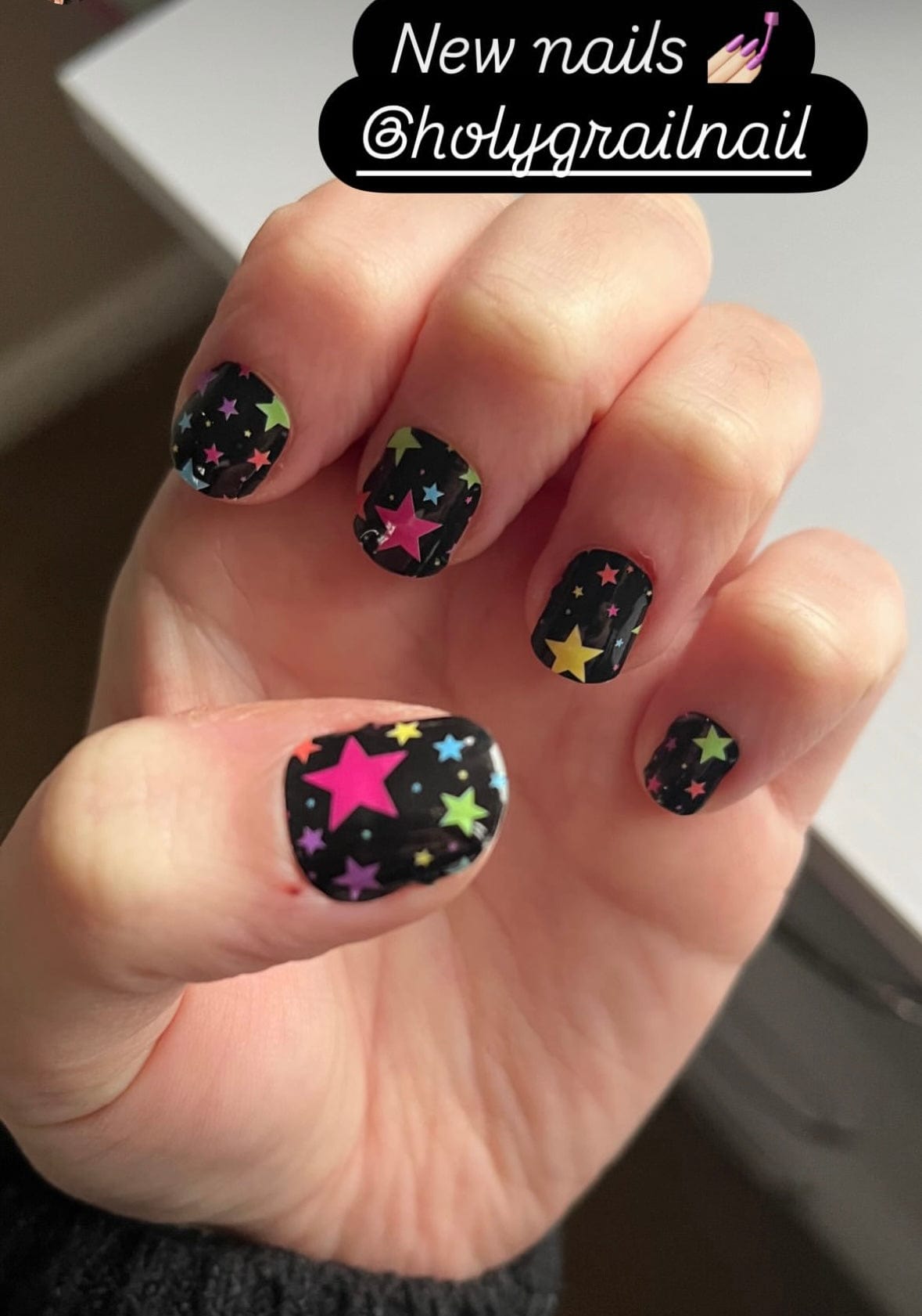 Black nail wraps with colourful rainbow stars on hand showing at-home manicure