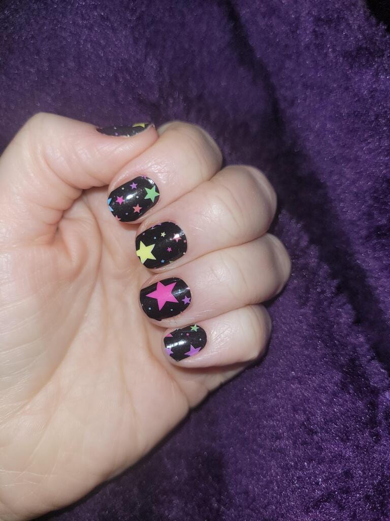 Non-UV nail wraps featuring bright multicoloured stars on black background on hand