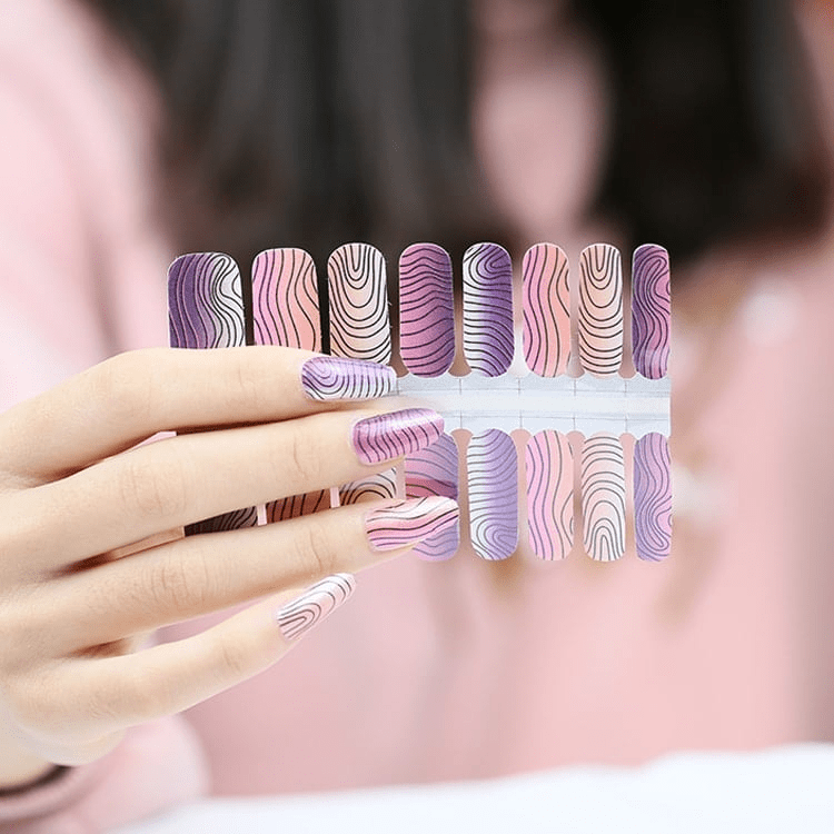 Hand wearing purple pink nail wraps with abstract wavy stripe nail art design