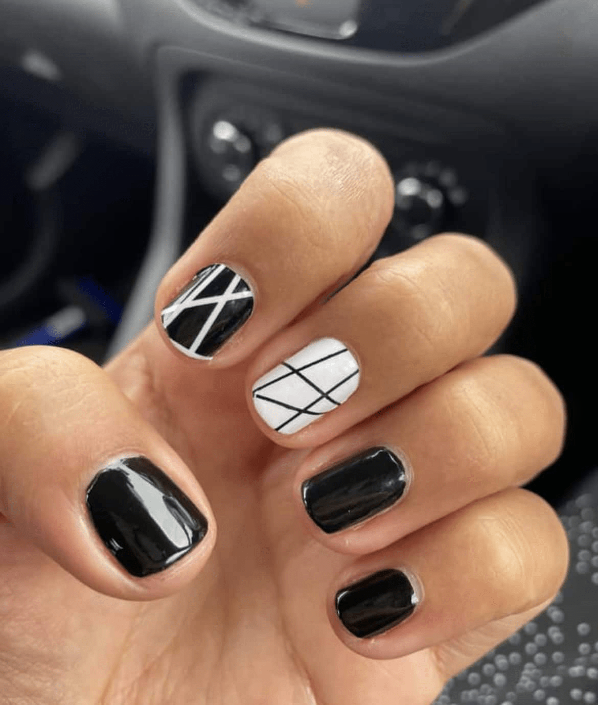 Hand displaying black and white geometric nail wraps with dramatic crosshatch grid pattern design