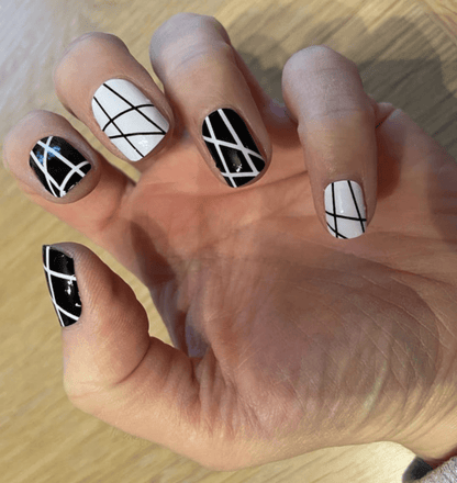 Hand showing monochrome nail wraps with bold black and white geometric crosshatch line nail art