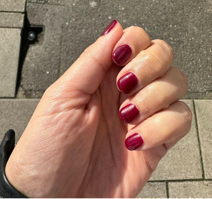 Deep wine-red nail wraps on short round nails, glossy finish, wide fit, on hand outdoors