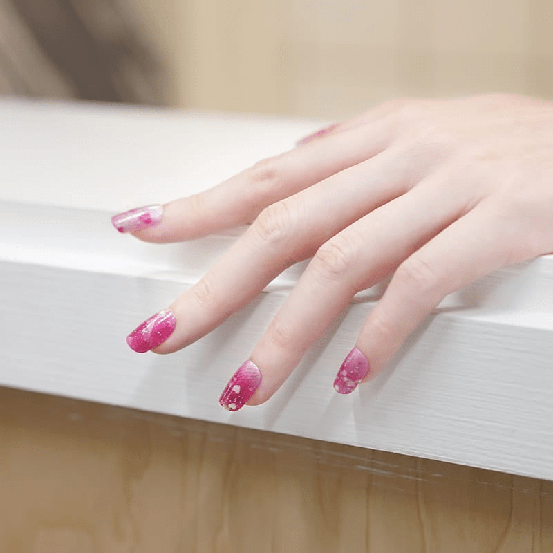 Hand displaying pink glittery heart nail wraps with ombre fade effect