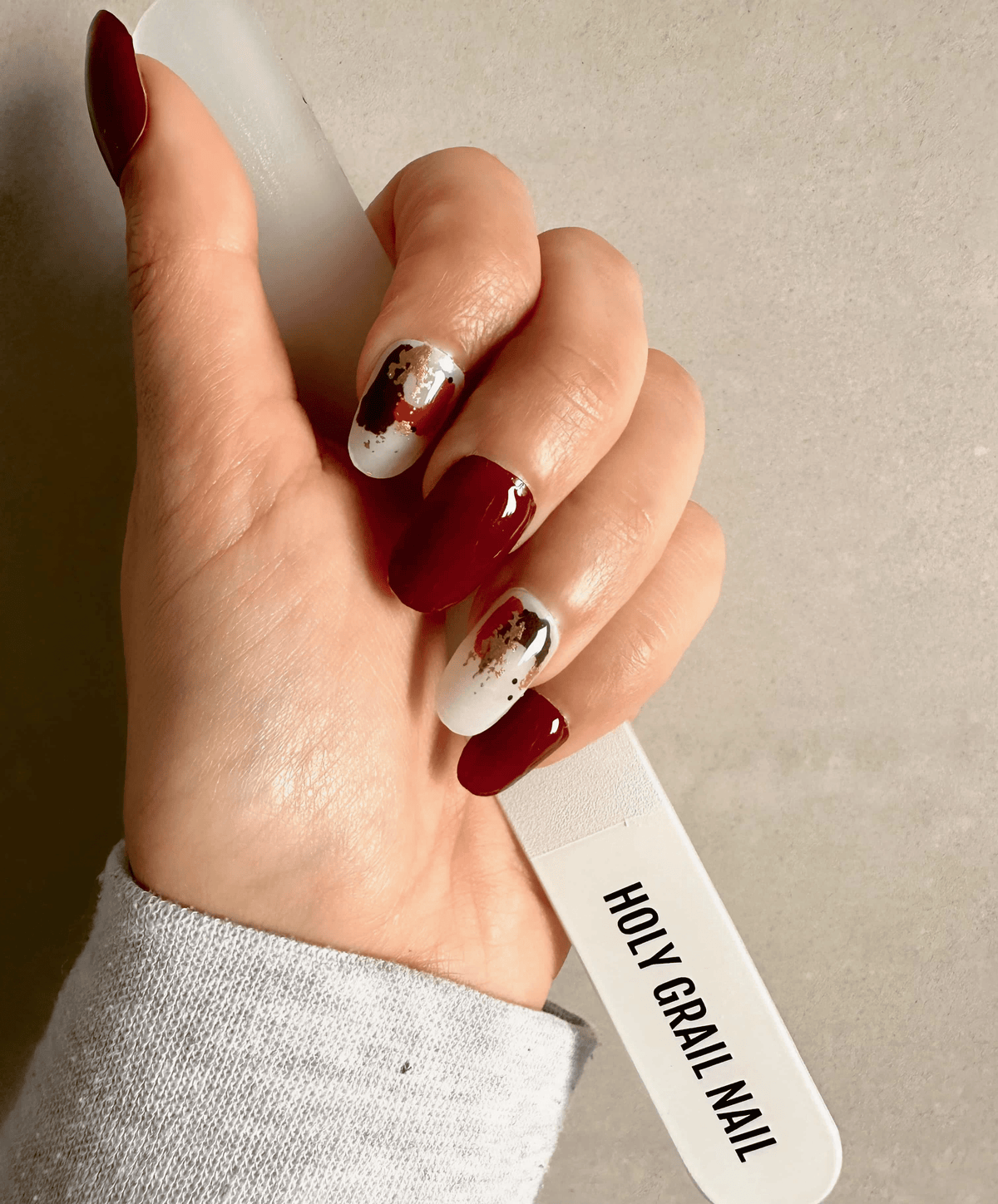Hand wearing burgundy and gold abstract nail wraps with paint splash artistic pattern
