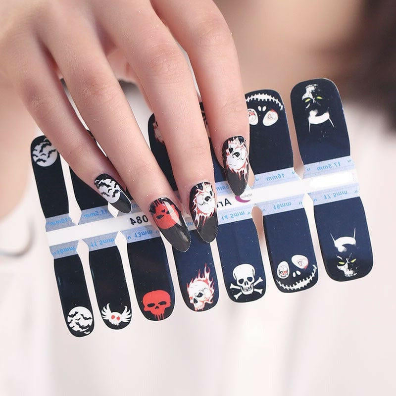 Hand wearing black nail wraps featuring white skulls and gothic Halloween nail art designs