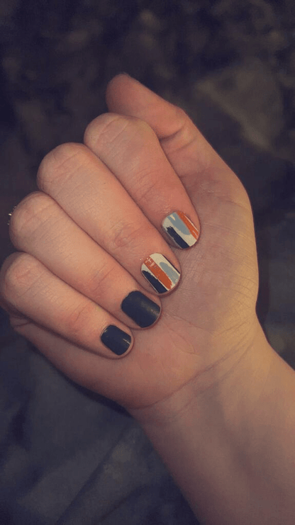 Hand showing navy blue and orange striped nail art using geometric nail wraps