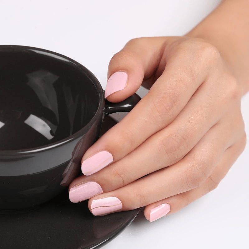 Hand wearing pink striped non-UV nail wraps holding black coffee cup