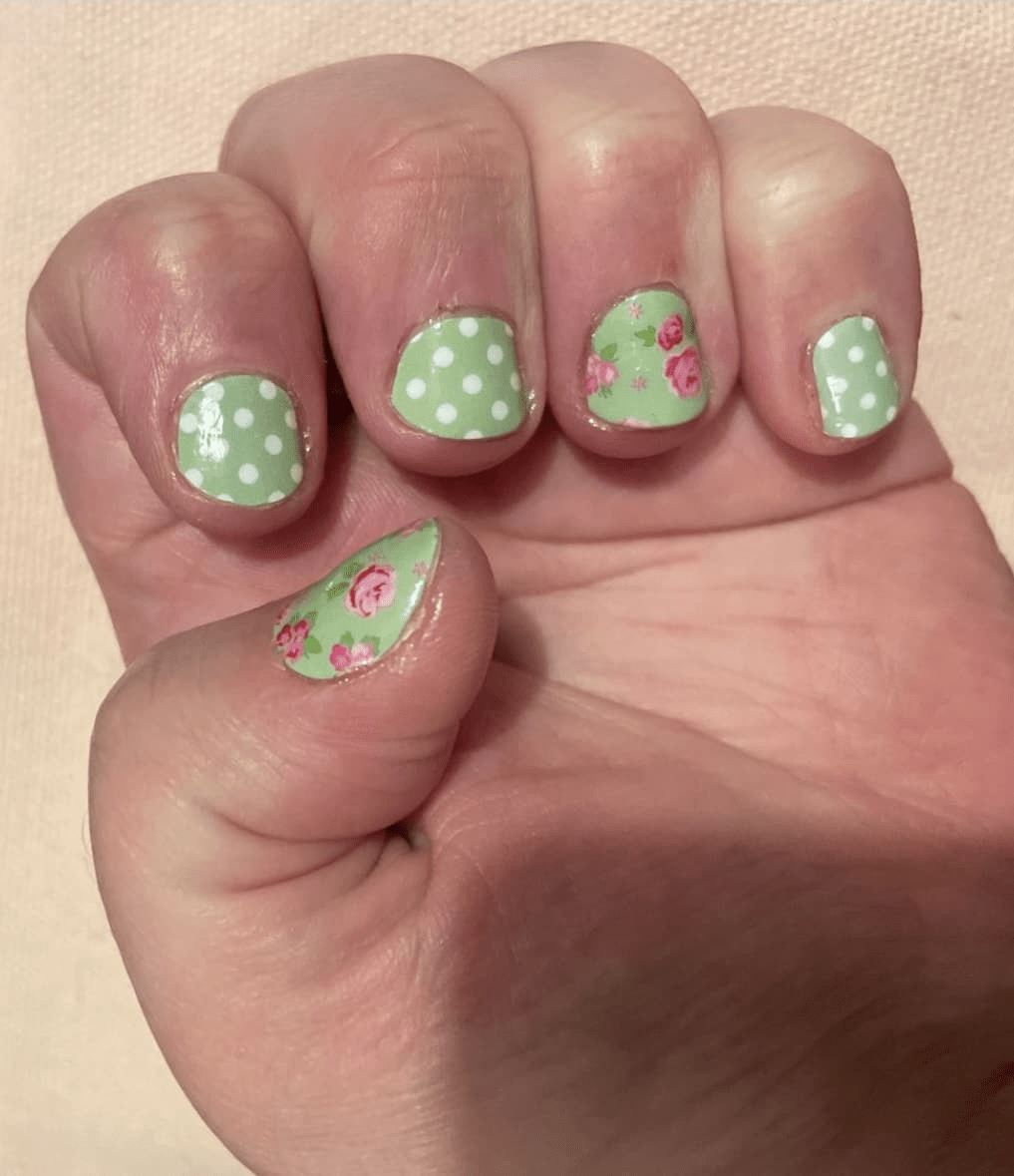 Hand displaying green nail art wraps featuring pink roses and white polka dots