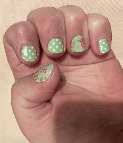 Hand displaying green nail art wraps featuring pink roses and white polka dots