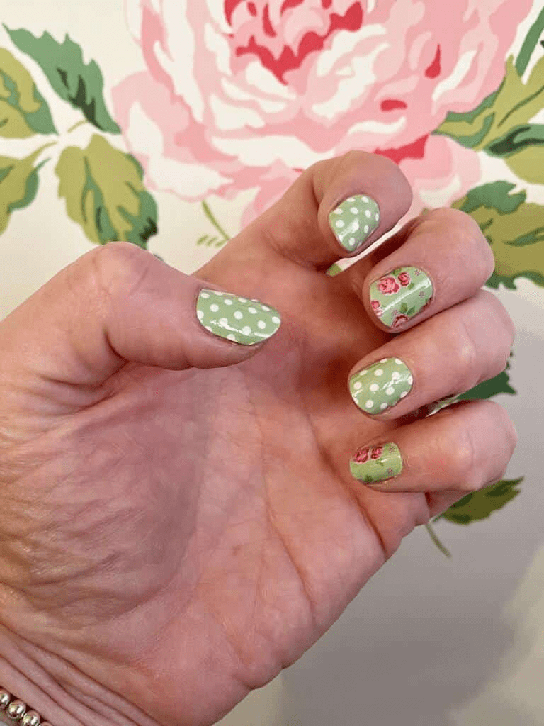 Hand wearing green floral nail wraps with pink roses and polka dot patterns