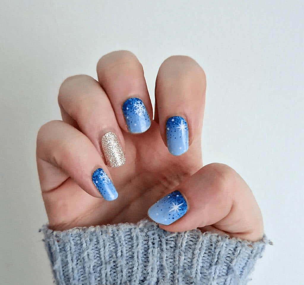 Blue snowflake nail wraps with gold accent nail on hand wearing grey knit jumper sleeve