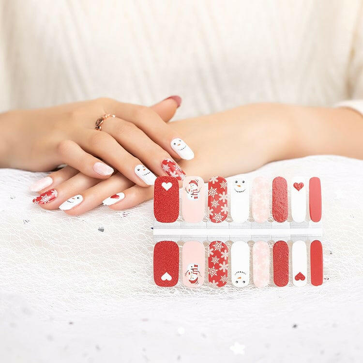 Hand wearing red and white Christmas nail wraps with snowman and heart designs