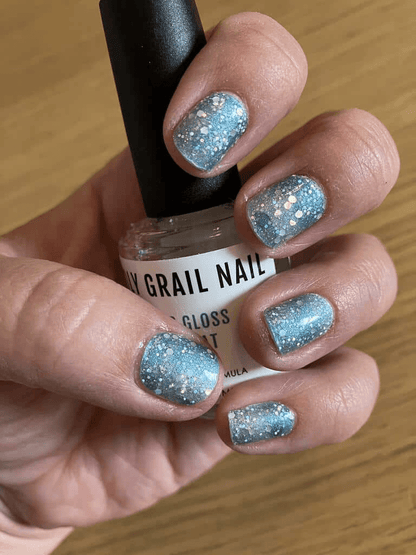 Close-up of blue sparkly glitter nail wraps on hand holding nail care bottle