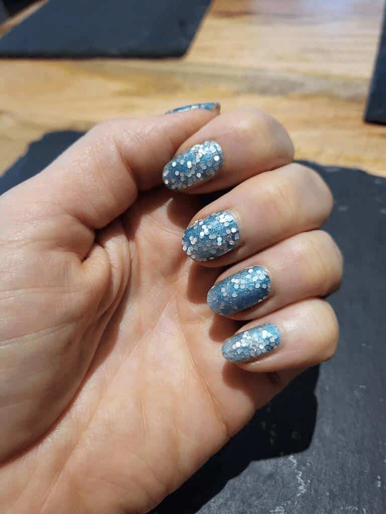 Hand displaying blue glitter nail wraps with winter sparkle pattern against dark background