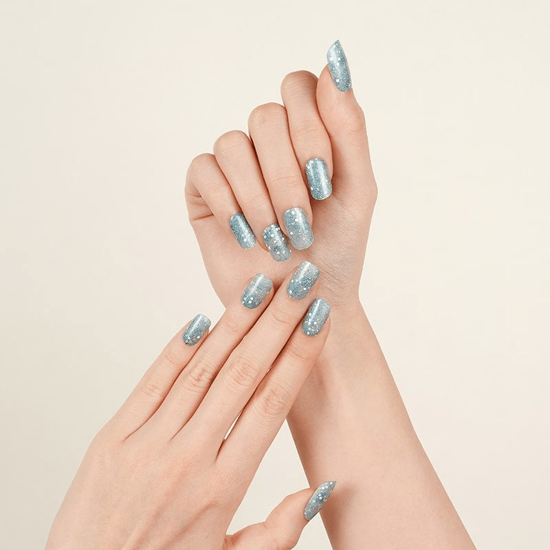 Two hands displaying blue glitter nail wraps with sparkly winter pattern manicure
