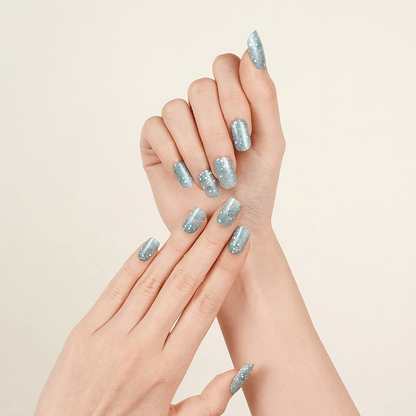 Two hands displaying blue glitter nail wraps with sparkly winter pattern manicure