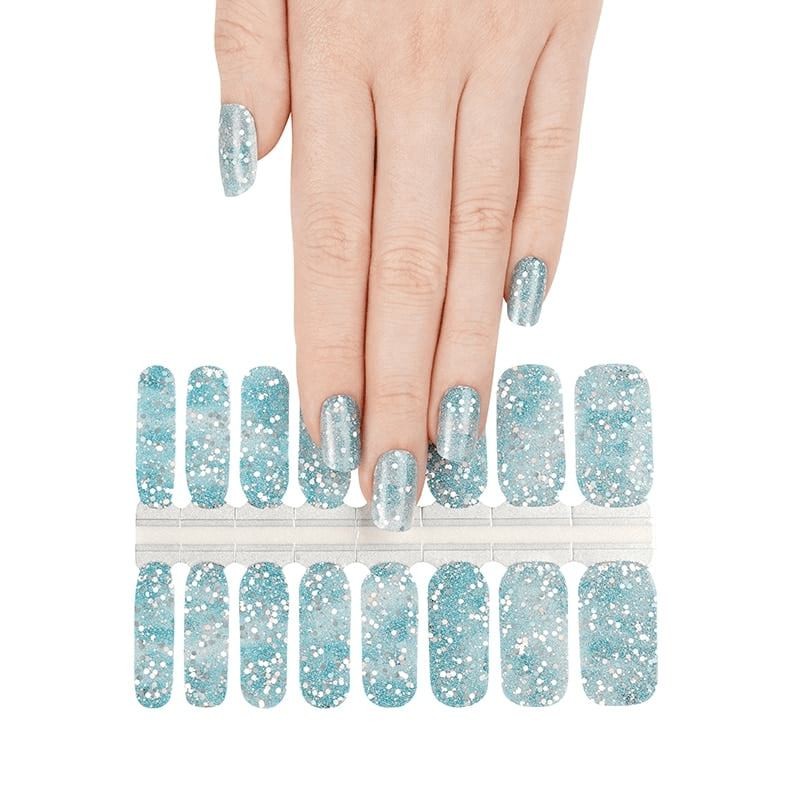 Hand wearing blue glitter nail wraps with nail wrap sheet showing winter sparkle design