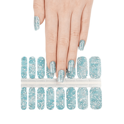 Hand wearing blue glitter nail wraps with nail wrap sheet showing winter sparkle design