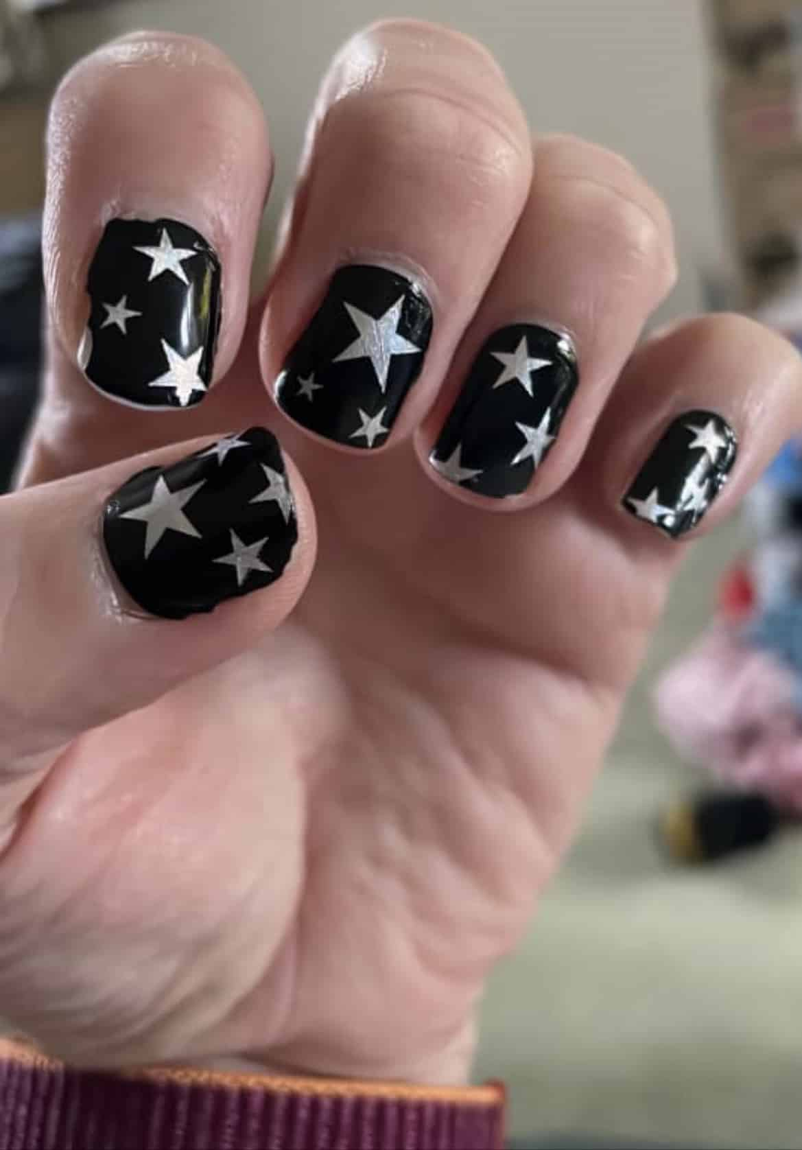 Hand displaying black nail wraps with silver stars celestial nail art design