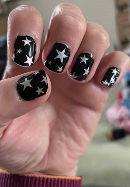 Hand displaying black nail wraps with silver stars celestial nail art design