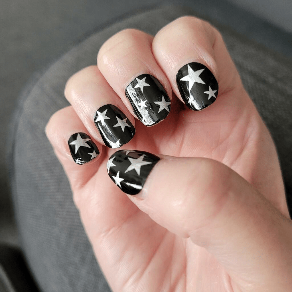 Black nail wraps with silver metallic stars on hand showing celestial nail art design