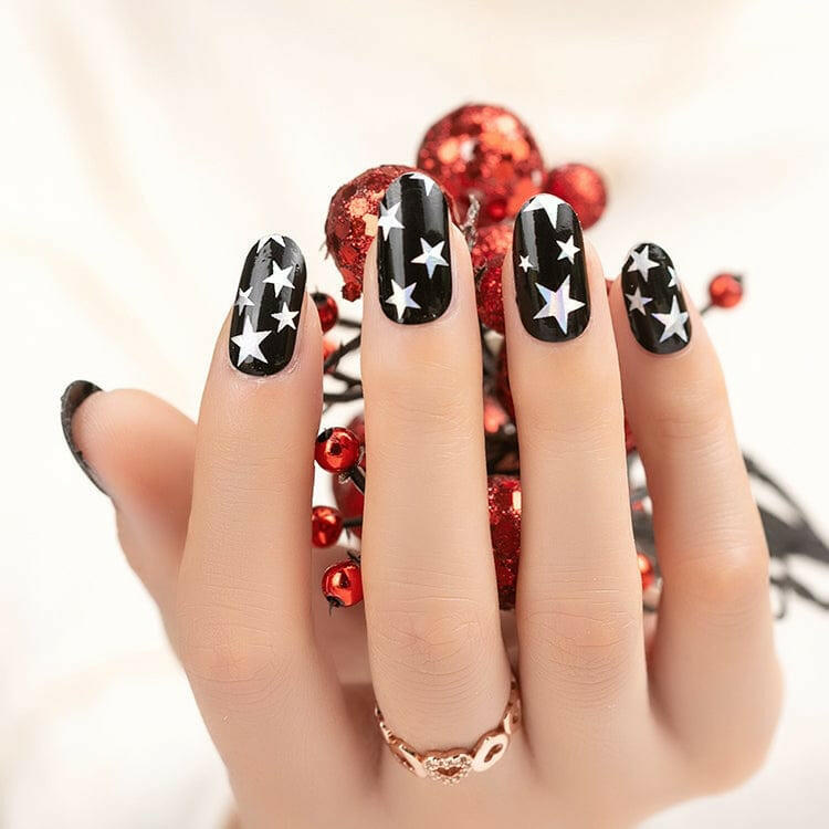 Hand wearing black nail wraps with metallic star pattern and red decorations