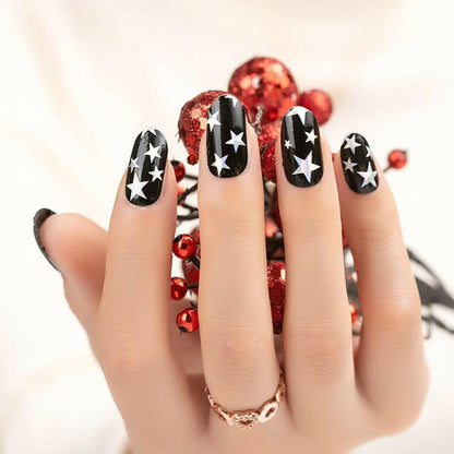 Hand wearing black nail wraps with metallic star pattern and red decorations