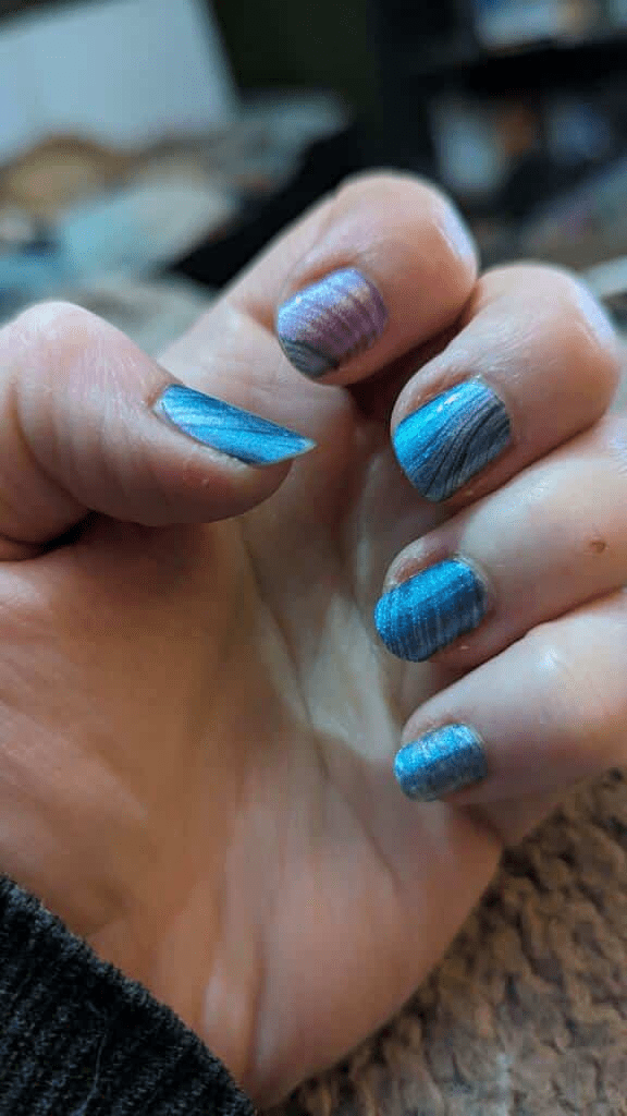 Hand wearing blue metallic wave nail wraps with abstract flowing pattern design
