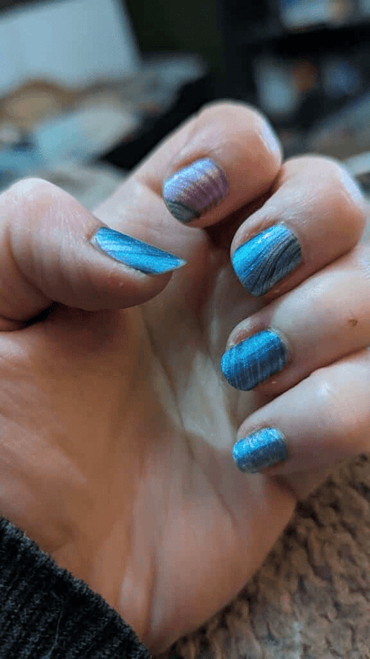 Hand wearing blue metallic wave nail wraps with abstract flowing pattern design