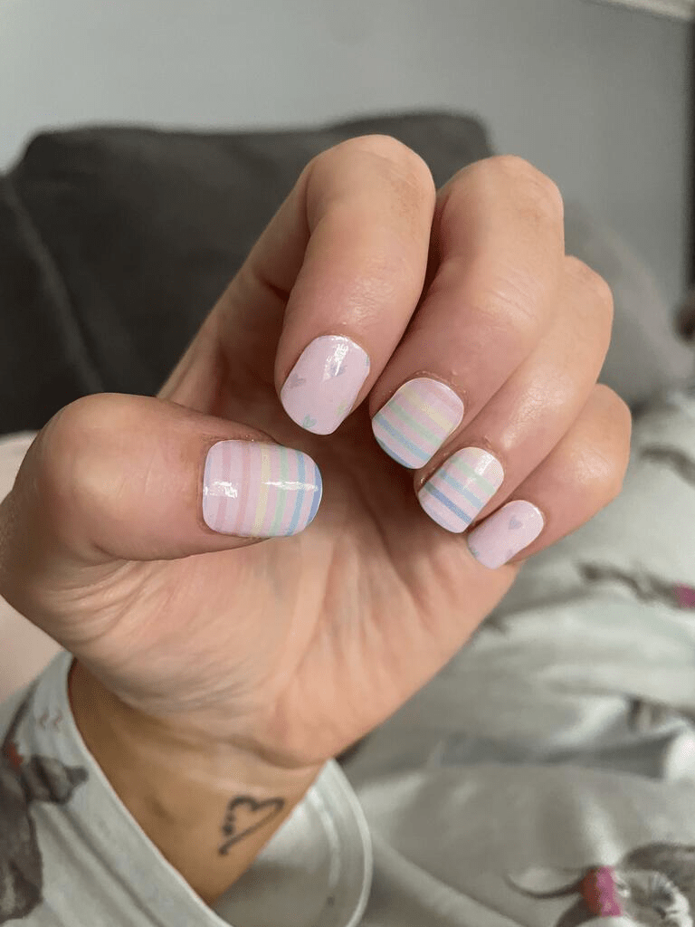 Hand wearing pink striped nail wraps with rainbow pastel colours for at-home manicure