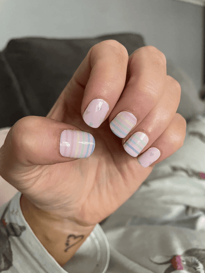 Hand wearing pink striped nail wraps with rainbow pastel colours for at-home manicure