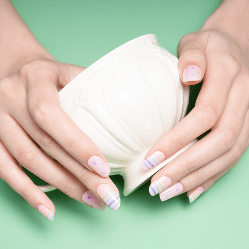 Hands holding white jar with pastel rainbow striped nail art wraps applied