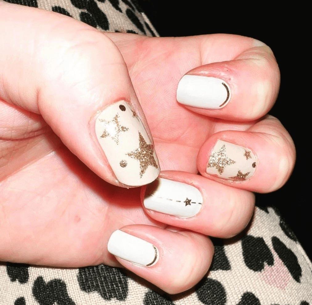 White and champagne nail wraps with gold glitter star pattern on hand