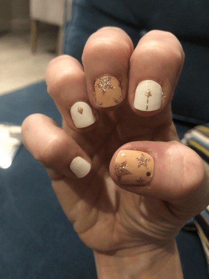 Hand displaying champagne and white nail wraps with sparkling gold star patterns celestial manicure