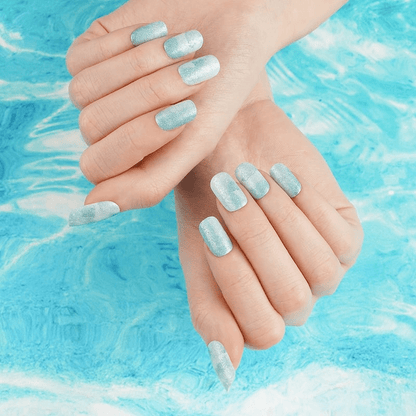 Hands wearing seafoam glitter nail wraps with marble shimmer against blue water background