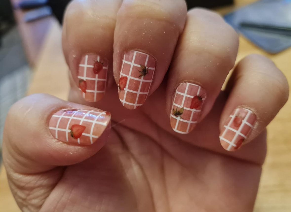 Nail wraps with white gingham grid pattern and strawberry motifs on sheer pink