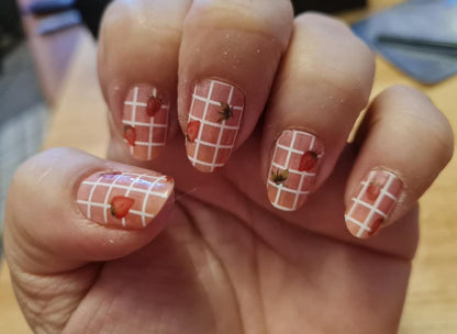 Nail wraps with white gingham grid pattern and strawberry motifs on sheer pink