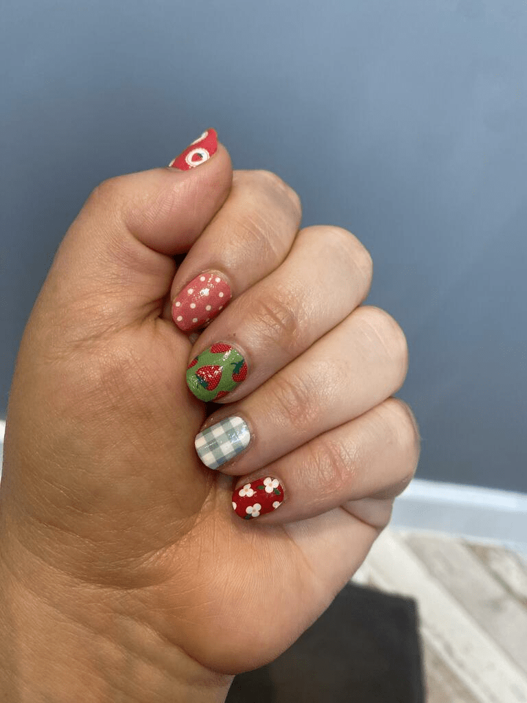 Hand wearing festive Christmas nail wraps with red strawberries, green gingham and white polka dots
