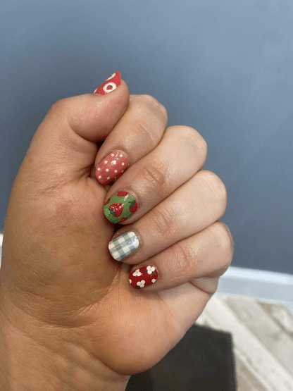 Hand wearing festive Christmas nail wraps with red strawberries, green gingham and white polka dots