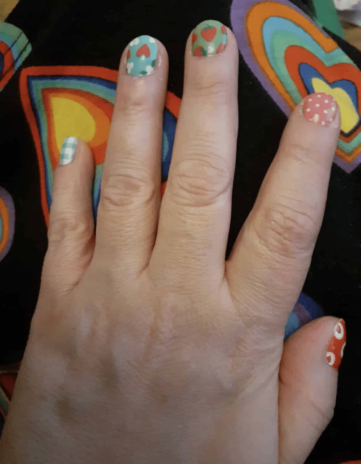 Hand showing Christmas themed non-UV nail wraps with strawberry and gingham patterns on colourful background