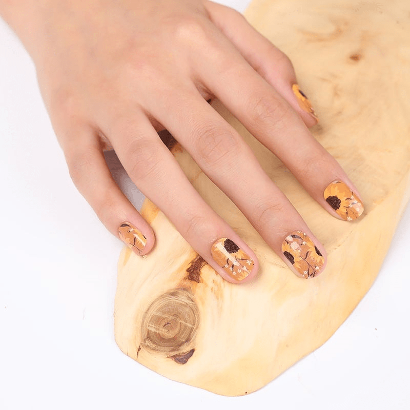 Hand wearing yellow sunflower nail wraps on wooden surface showing floral manicure