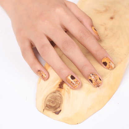 Hand wearing yellow sunflower nail wraps on wooden surface showing floral manicure