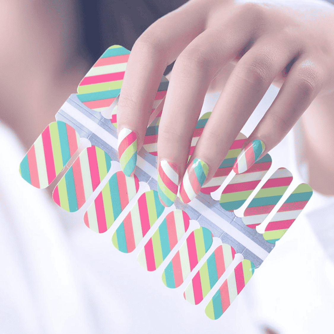 Hand holding multicoloured striped nail wraps with diagonal pink coral green patterns